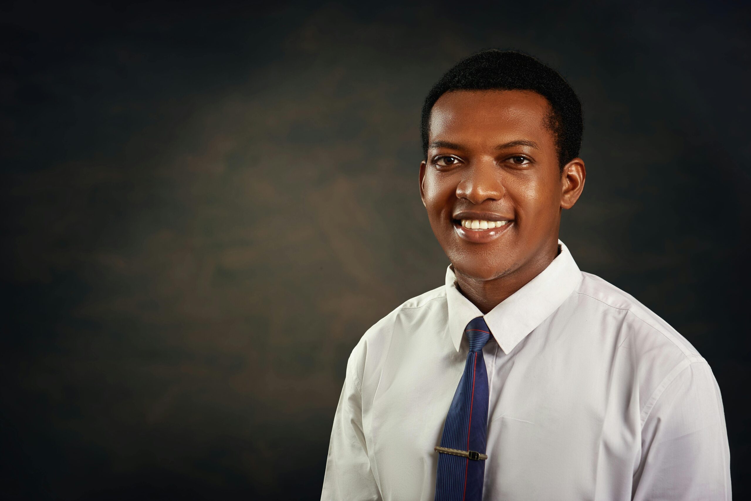 Smiling young adult man in formal attire against dark background, ideal for business or profile use.